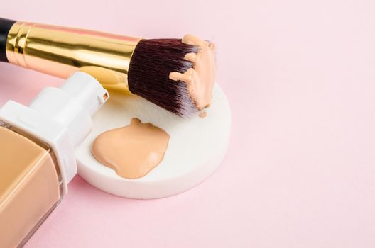 The Liquid fluid foundation glass bottle on makeup sponges and brush makeup on pink background.