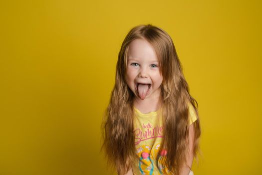Portrait of beautiful little girl with long hair smiling posing isolated at yellow studio background medium shot. Happy cute European female child having fun looking at camera feeling positive emotion