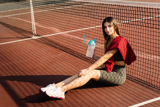 Athletic fit Asian girl drinking water from a bottle. Rest after training on the tennis court