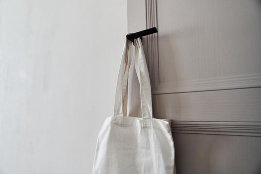 Eco friendly concept with white canvas tote bag hanging on door knob with two toned colored, Eco blank shopping sack with free copy space, Reduce plastic bags to reduce global warming. Canvas tote bag