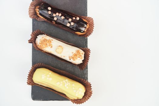 Three eclairs on a black tray top view. Traditional French dessert