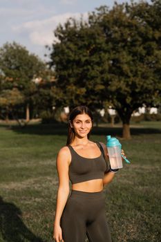 Fit sports model is resting after training and drinking water from a bottle in green park. Sports lifestyle