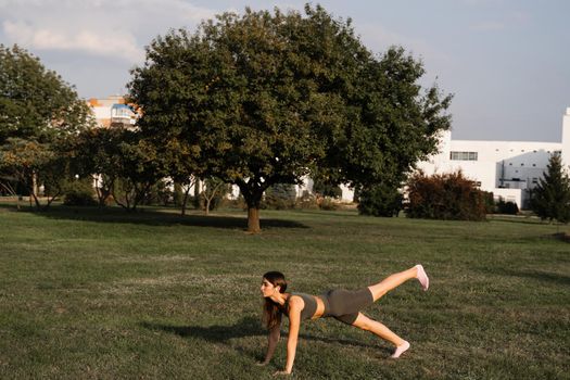 Fit girl does warm-up and stretching exercises in green park. Sports lifestyle