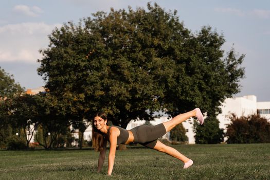 Fit girl training on green grass in the park. Outdoor workout. Sport lifestyle of active young woman