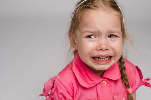 Little girl in pink shirt looking aside and crying on isolated background. Scared sad child screaming in studio. Unhappy kid weeping. Concept of violence, offense and childhood.