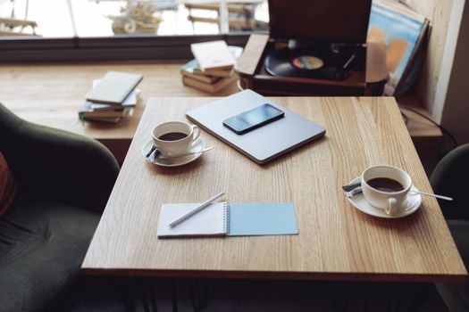 Wooden table with two white cups of coffee and business stuff. Cozy place for meeting in cafeteria.