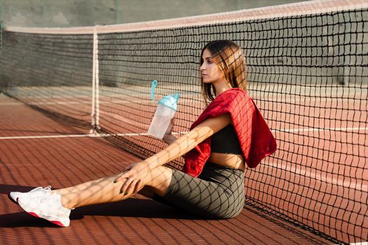 Athletic fit Asian girl drinking water from a bottle. Rest after training on the tennis court