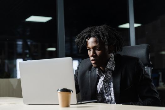 Black IT programmer is working on laptop in coworking space. Handsome african man with laptop in the office