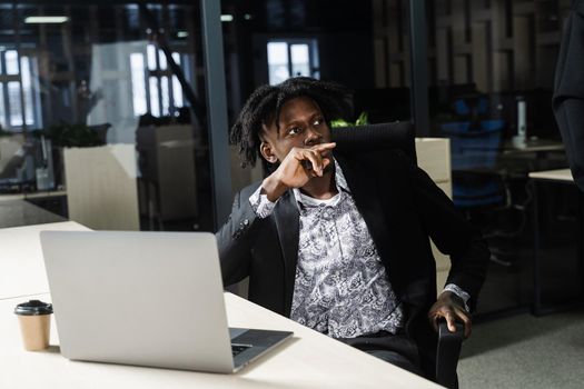 Black hipster man with laptop is listening a speech of his colleagues. Teamwork. Offline job