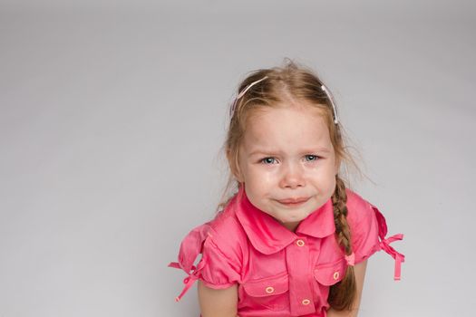 Little girl in pink shirt looking aside and crying on isolated background. Scared sad child screaming in studio. Unhappy kid weeping. Concept of violence, offense and childhood.