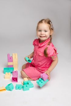 Stock photo portrait of lovely little girl holding high colored blocks constructed by herself. Cute smiling girl playing with plastic colorful blocks in studio. She is smiling at camera happily.