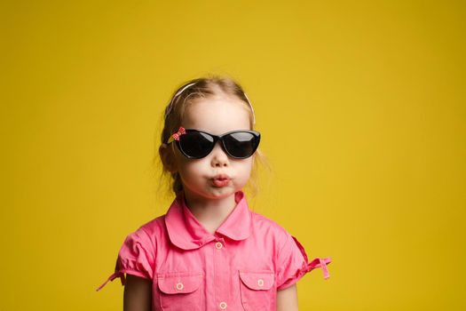 Stock photo portrait of adorable little kid in fashionable black sunglasses pouting her lips funnily on yellow background. Isolate.