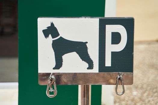 Designated dog parking sign on blue plate. Place for bind dogs waiting for owners outside, with rings for attaching leash, on public place area or shop. Copy space. Close-up. Outdoors.