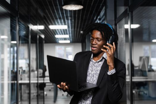 Cheerful black man in headphones listen audio podcast and enjoy music. Handsome african man with laptop in the office. Party concept