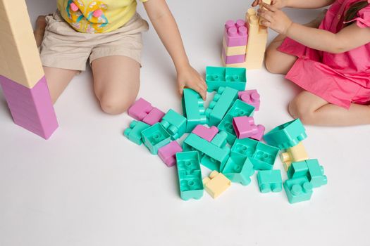Two enthusiastic little girl playing assemble constructor full shot at studio white background. Little cute female child friend building tower using cubes enjoying childhood together
