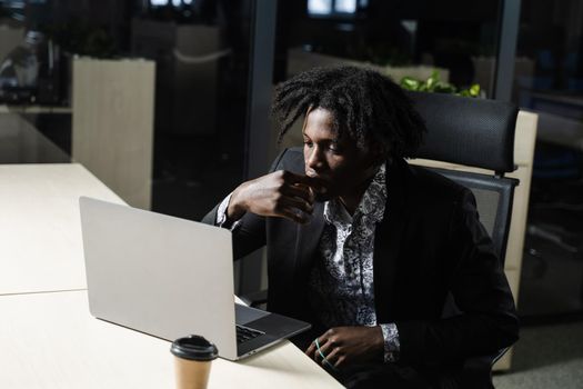 Black IT programmer is working on laptop in coworking space. Handsome african man with laptop in the office