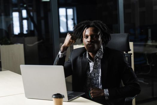 Happy black man clenched fists and rejoice finishing his online job on laptop. Working online in coworking space