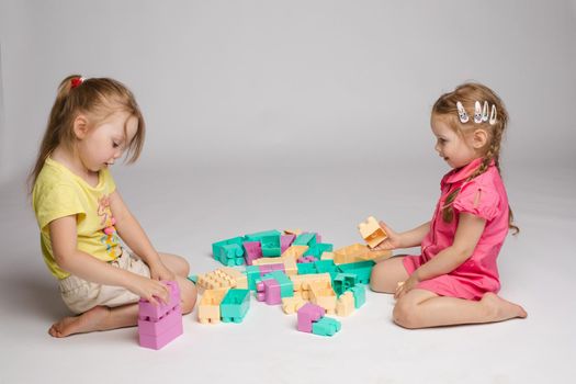 Two enthusiastic little girl playing assemble constructor full shot at studio white background. Little cute female child friend building tower using cubes enjoying childhood together
