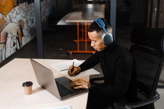 Handsome asian student writes notes and doing distance learning online. Remote work for programmers with laptop and headphones