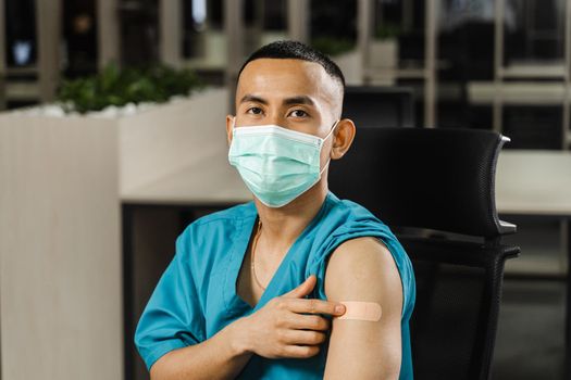 Handsome asian man vaccinated against coronavarus and showing patch on his arm. Covid-19 vaccination. Filipino man in medical mask.