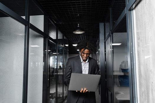 Focused young black businessman working online on laptop in office. Remote work.