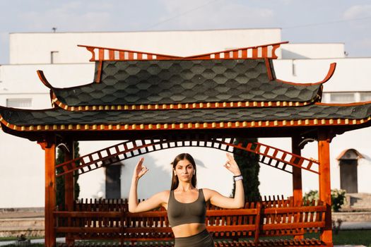 Asian fit girl meditates against the background of a Chinese gazebo. Relaxation and meditation outdoors