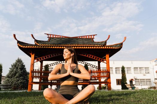 Praying and meditation in lotus position. Fit girl is sitting and meditating outdoors near chinese gazebo