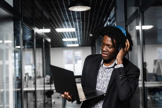 Cheerful black man in headphones listen audio podcast and enjoy music. Handsome african man with laptop in the office. Party concept