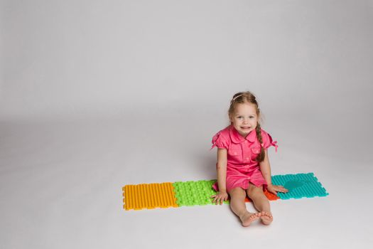 Stock photo of a child playing with colorful bright rubber pads for improving and developing fine motor skills on the floor. She is sitting on her haunches in studio.