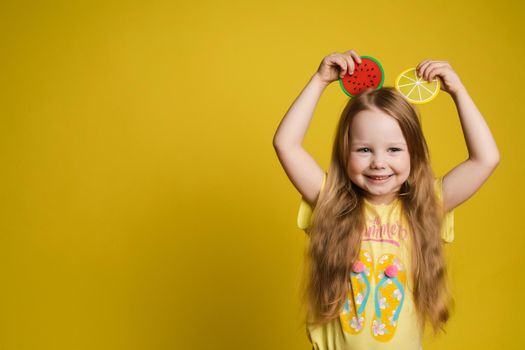 Happy cute little child girl holding slice of fruit over head making ears having fun medium close-up. Smiling beautiful female kid feeling positive emotion posing isolated at yellow studio background