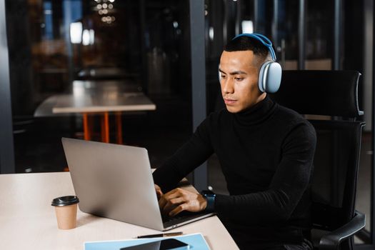 Asian man in headphones working online and listen to music in office. Asian handsome guy with laptop in coworking space