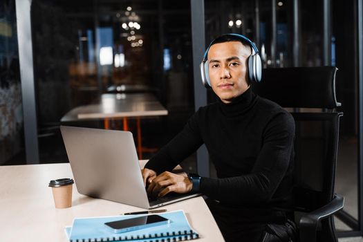 Handsome asian student with laptop and headphones is doing distance learning online. Remote work for programmers