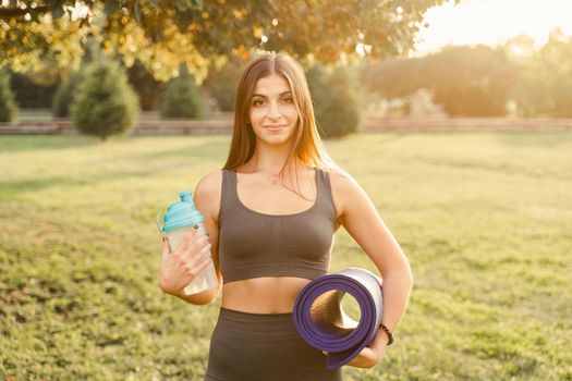 Athletic fit girl with training mat and bottle of water outdoor. Advertising for a sports nutrition and equipment store