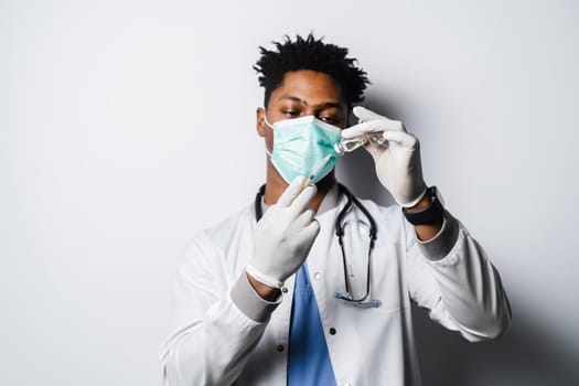 African doctor in a medical mask prepares to give an injection of a coronavirus covid-19 vaccine. Black man in medical mask is making vaccination on white background