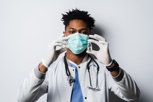 Handsome African doctor with coronavirus covid-19 vaccine. Black doctor in medical mask is holding vaccine on white background