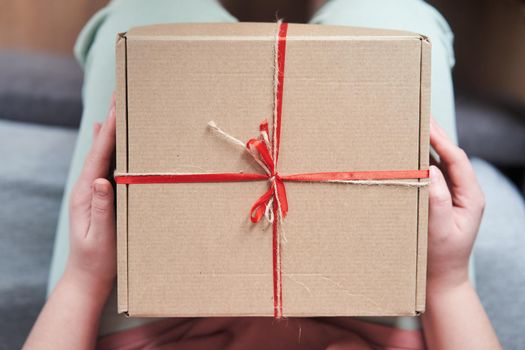 Selected focus. Girl holding a gift box with a red ribbon in her hands. The girl received a gift