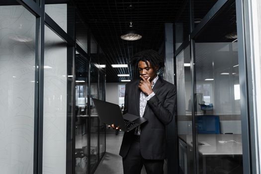 Confident black business man with laptop working online with his colleagues. Handsome african manager in the office