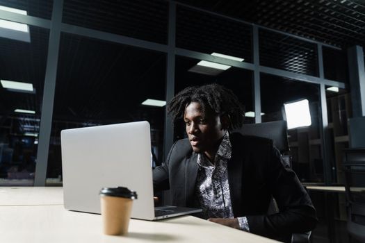 Black business man with laptop is working online in the office. Handsome african manager is doing remote work in coworking space