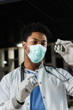 Black doctor with 3 doses of vaccine. Booster vaccination. African doctor in medical mask is holding vaccines in hand