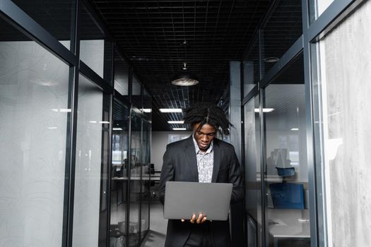 Focused young black businessman working online on laptop in office. Remote work