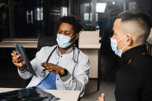 Asian patient at African doctor appointment. Fracture of the bones of foot. Black surgeon showing x-ray to patient