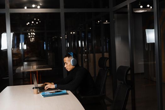 Asian man in headphones working online and listen to music in office. Asian handsome guy with laptop in coworking space