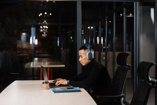 Asian man in headphones working online and listen to music in office. Asian handsome guy with laptop in coworking space