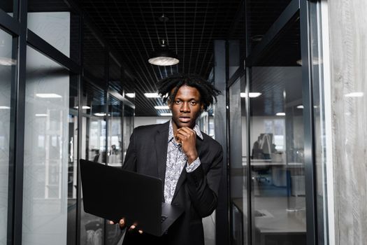 Confident black business man with laptop working online with his colleagues. Handsome african manager in the office