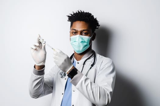 African doctor with coronavirus covid-19 vaccine in syringe. Black man in medical mask is making vaccination on white background