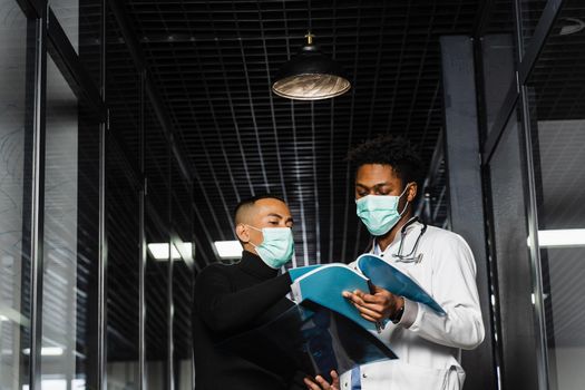 Asian patient with x-rays asks an African doctor about treatment of pneumonia and pleurisy. Black surgeon consult and help Asian man