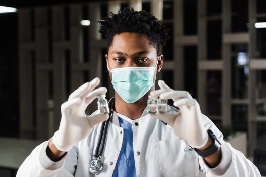 Black doctor with 3 doses of vaccine. Booster vaccination. African doctor in medical mask is holding vaccines in hand