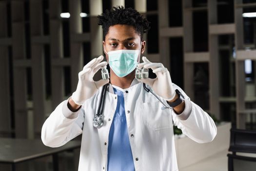 Black doctor with 3 doses of vaccine. Booster vaccination. African doctor in medical mask is holding vaccines in hand