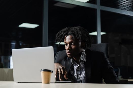 Black IT programmer is working on laptop in coworking space. Handsome african man with laptop in the office