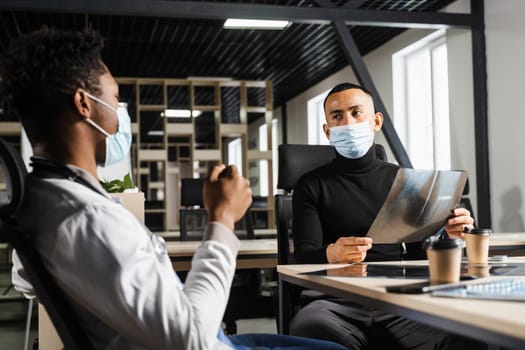 Asian patient is consulting a black surgeon doctor and discussing x-ray picture. Preparation for the operation. African doctor examining a patient